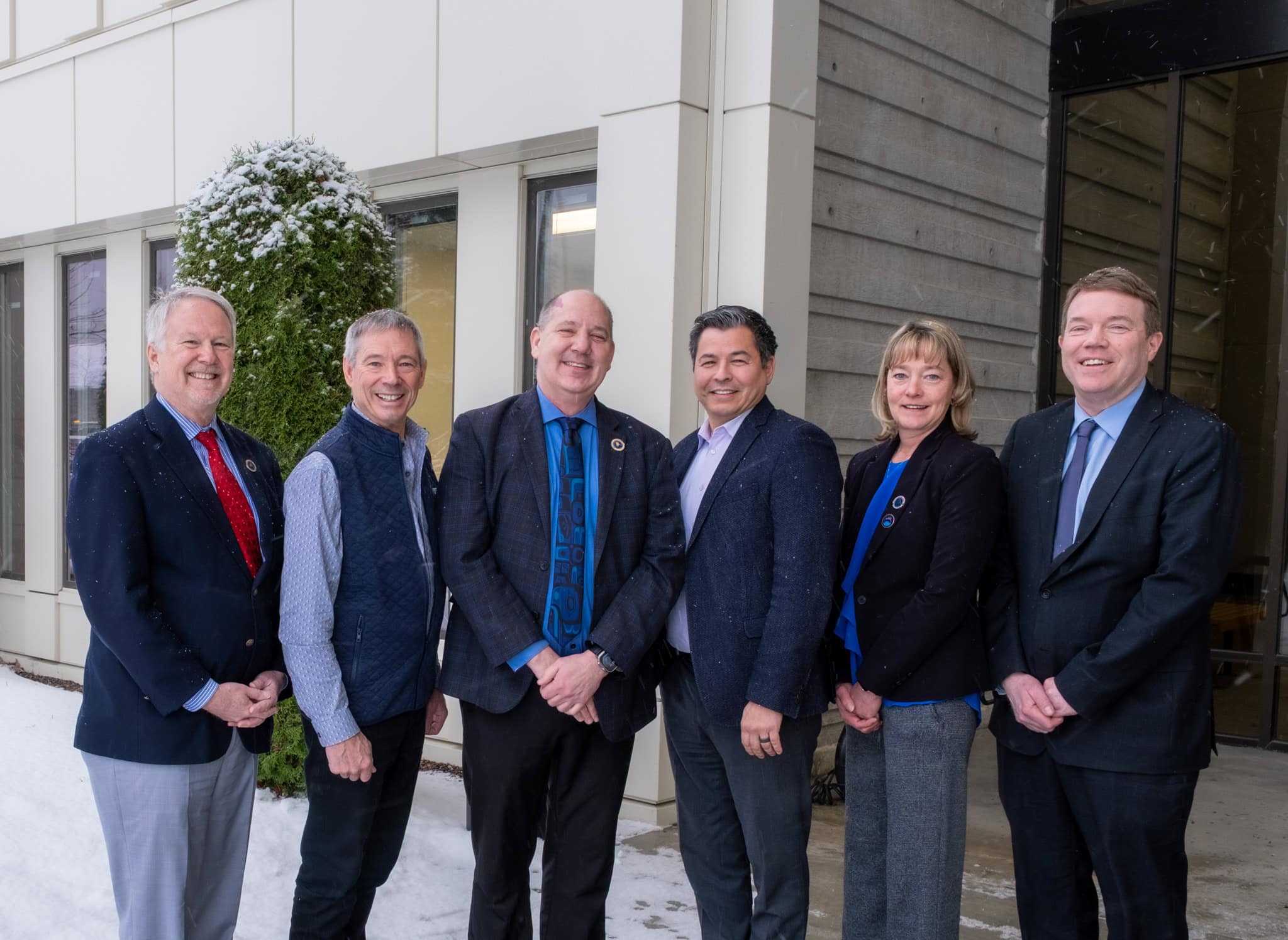 six people standing in front of a building smiling