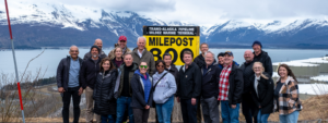 Staff members standing at the 800 mile marker sign of the Trans Alaska Pipeline in Valdez, AK