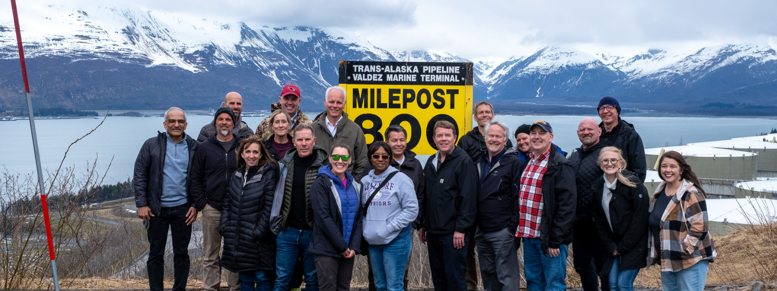 Staff members standing at the 800 mile marker sign of the Trans Alaska Pipeline in Valdez, AK 